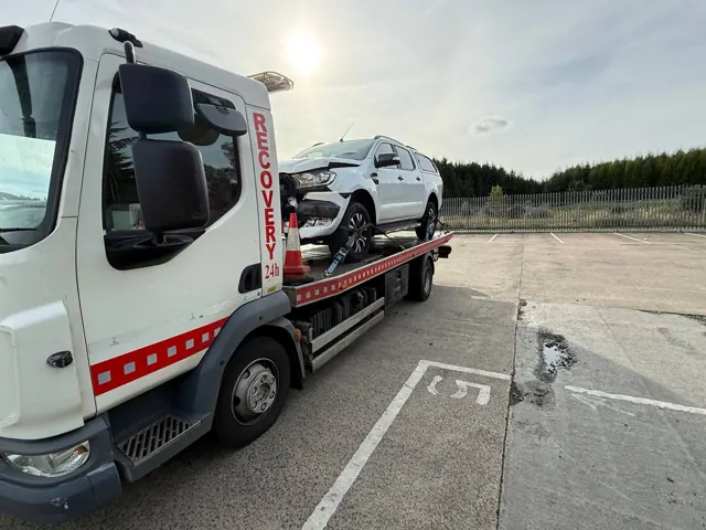 Accident-damaged white vehicle on a flatbed